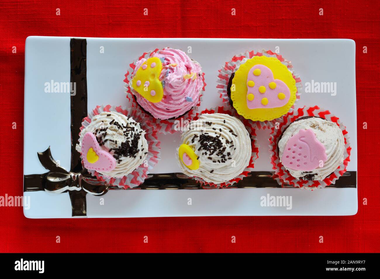 Amore muffin, colorato tortine decorate con cuori di marzapane servita in ceramica bianca piattino, vista da sopra Foto Stock