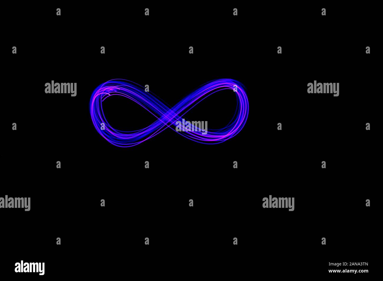 Lungo la luce di esposizione di pittura, vibrante di colore viola in un infinità di forma swirl simbolo contro un pulito sfondo nero. La pittura di luce la fotografia. Foto Stock