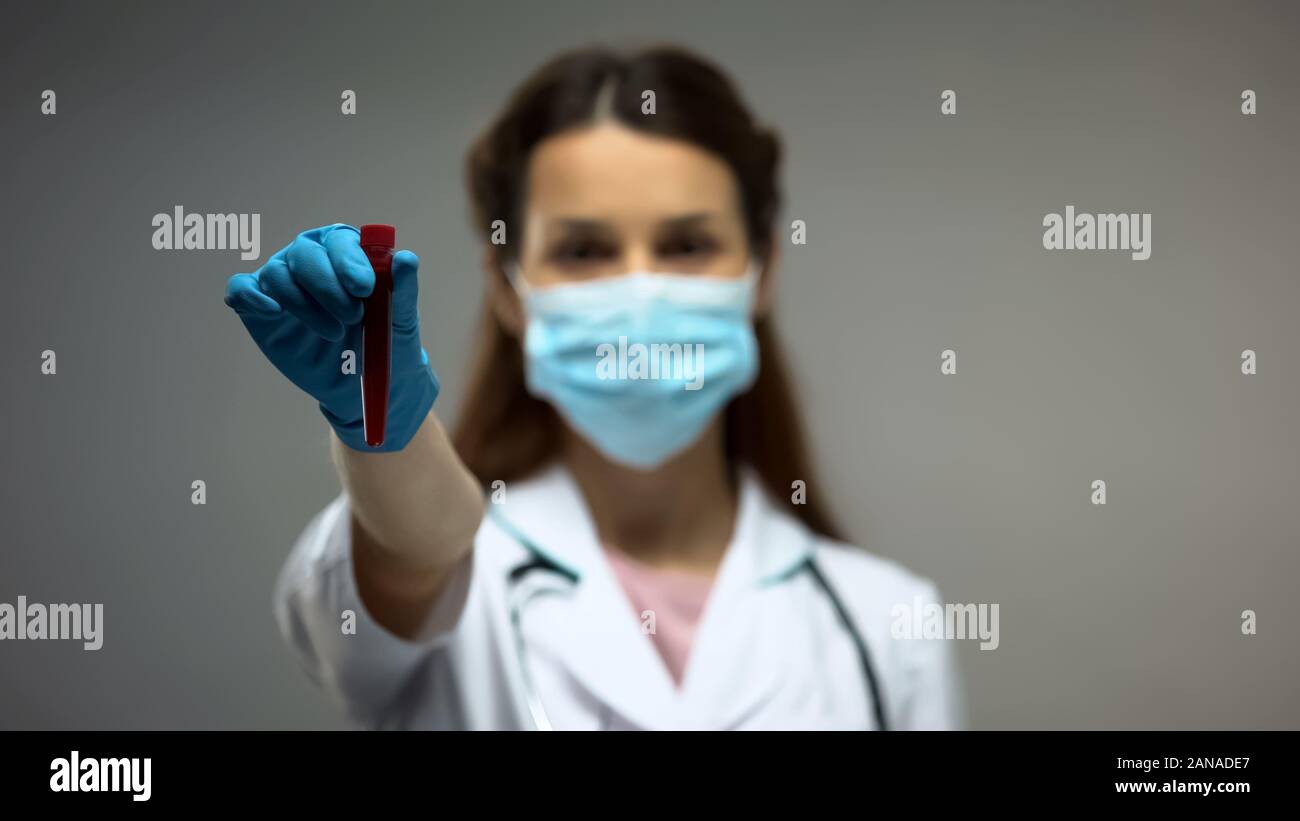 Ricercatore in maschera protettiva che mostra il tubo con i campioni di sangue, le epidemie Foto Stock