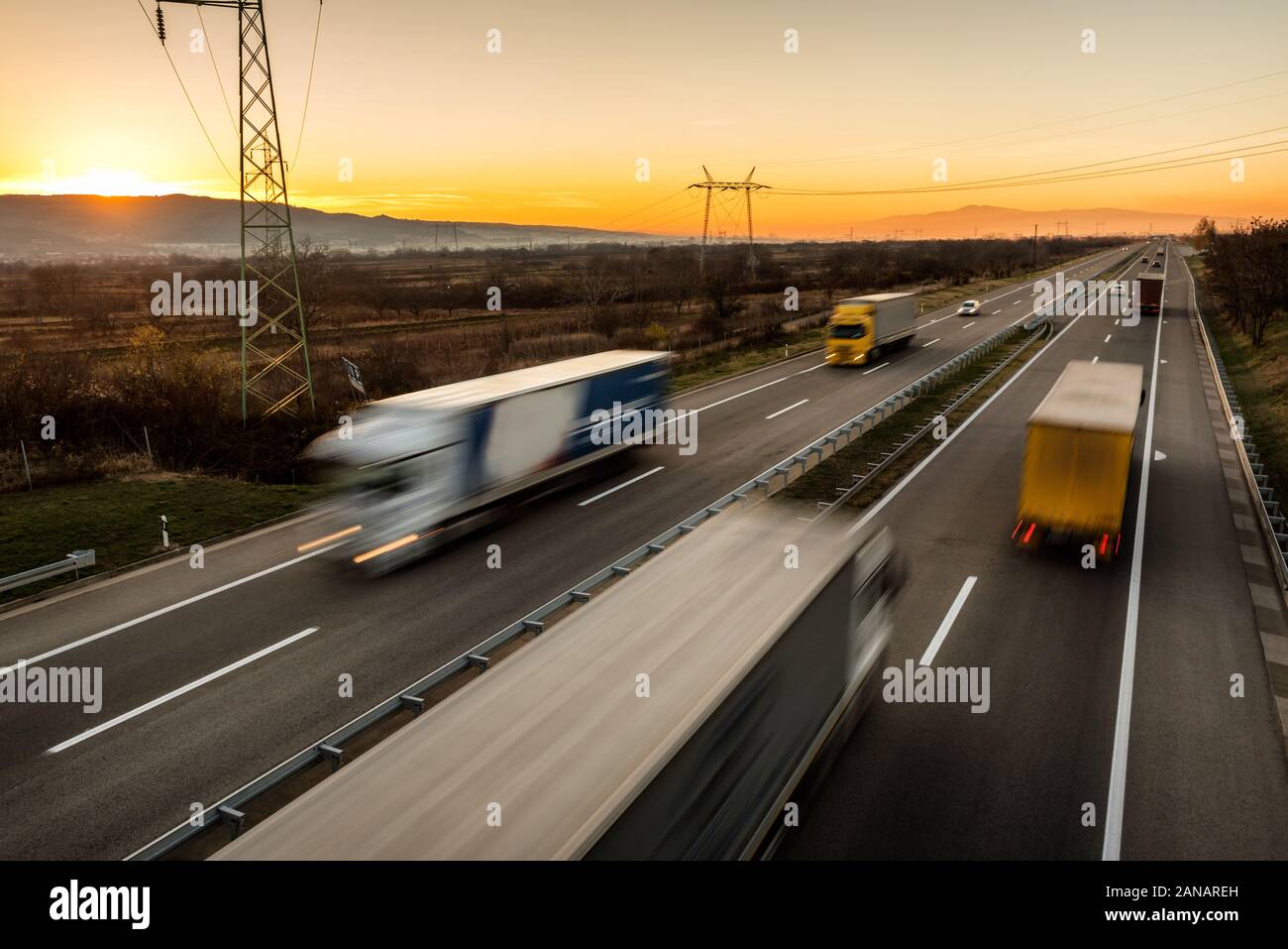 Consegna di camion e auto in alta velocità di guida su un'autostrada attraverso il paesaggio rurale. Guida in movimento veloce e sfocata sulla superstrada. La scena del trasporto sul mo Foto Stock