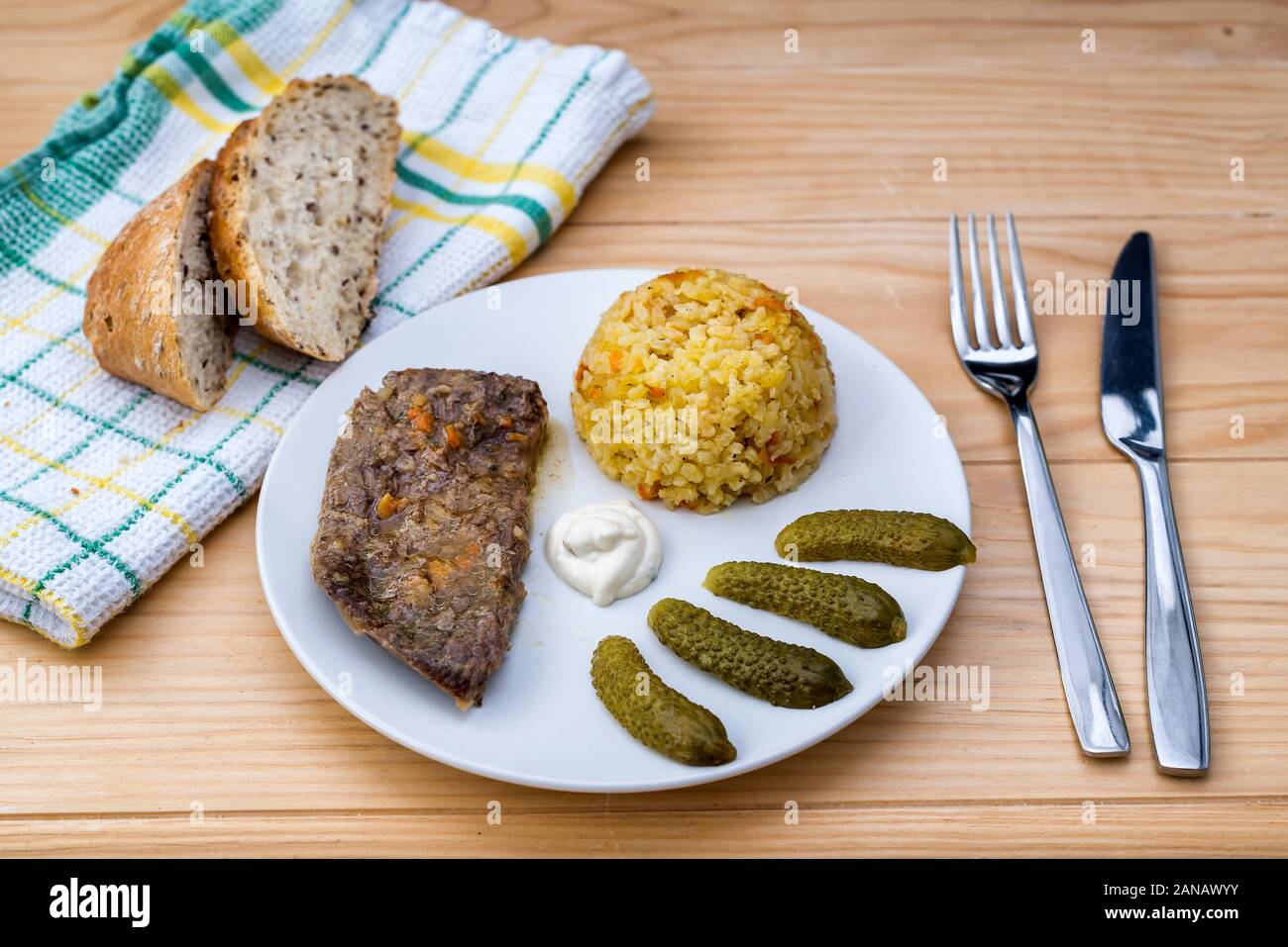 Preparate la bistecca di manzo con riso risotto, sottaceti e salsa su piastra bianca sul tavolo di legno sfondo Foto Stock