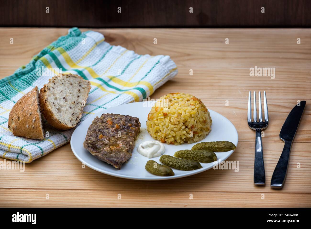 Preparate la bistecca di manzo con riso risotto, sottaceti e salsa su piastra bianca sul tavolo di legno sfondo Foto Stock
