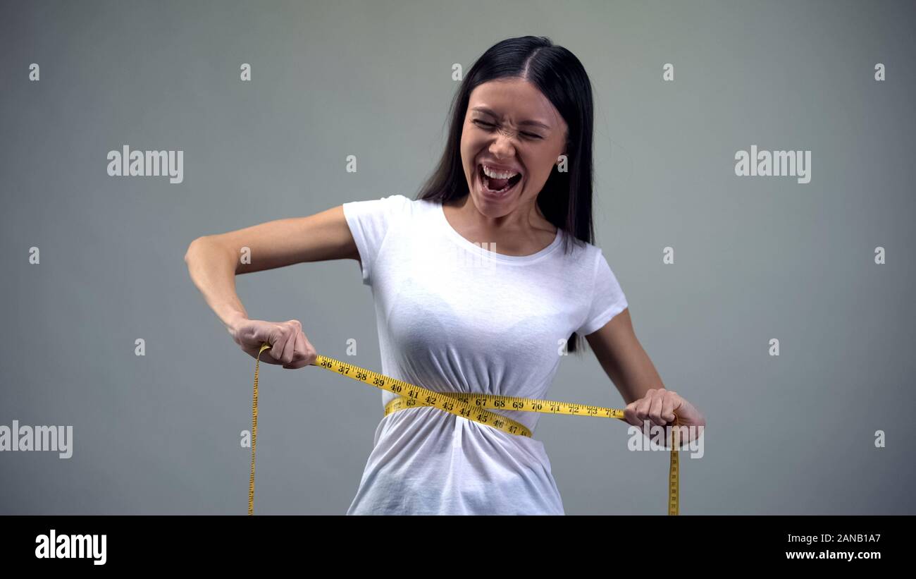 Giovane donna di serraggio del nastro di misurazione, torturare se stessa con la dieta, bulimia Foto Stock