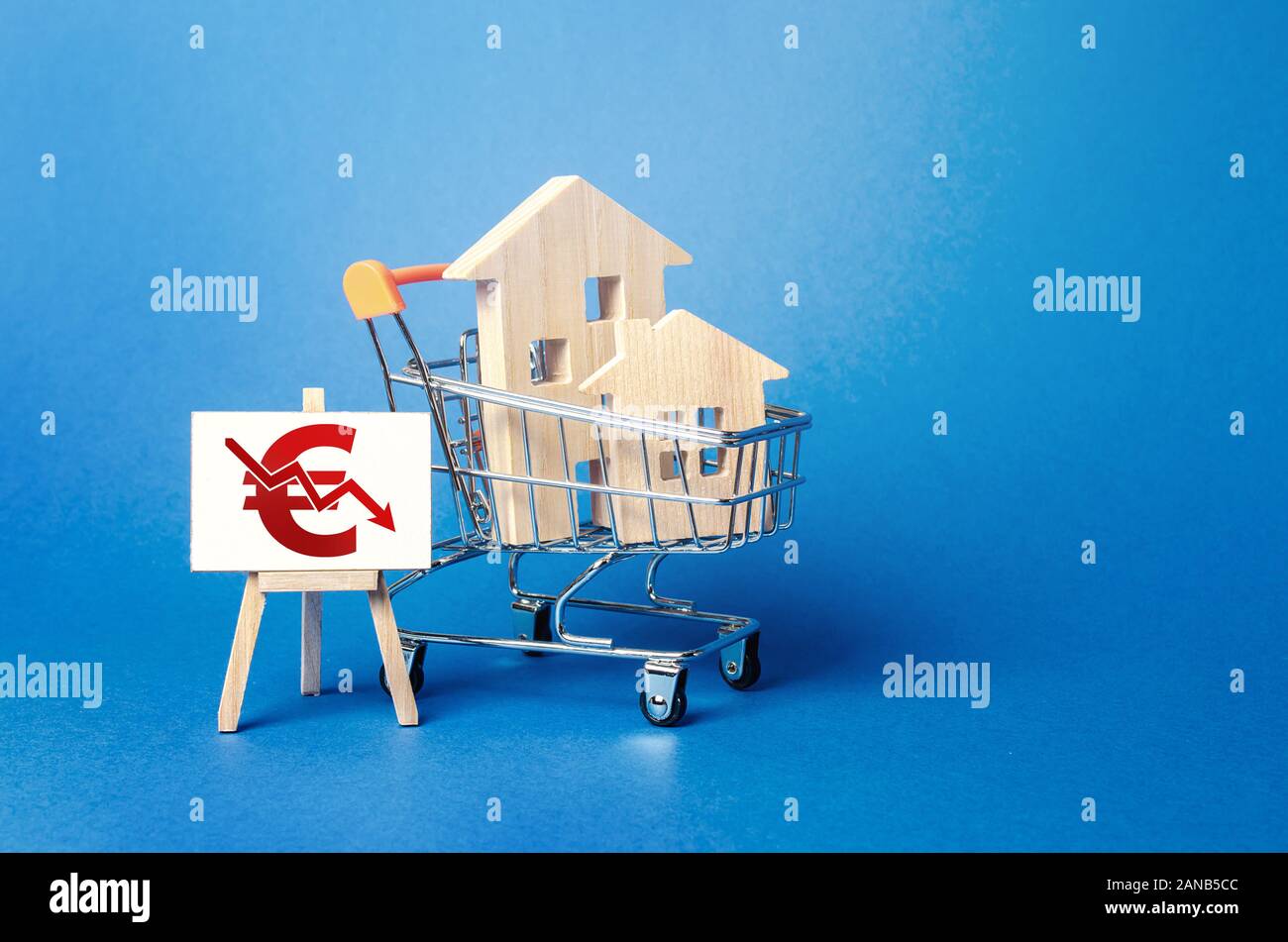 Case di legno in un carrello della spesa e un cavalletto con un rosso euro freccia giù grafico. Basso livello di vendite. Valore di diminuzione dei costi. Bad attrattiva. Caduta del real estat Foto Stock