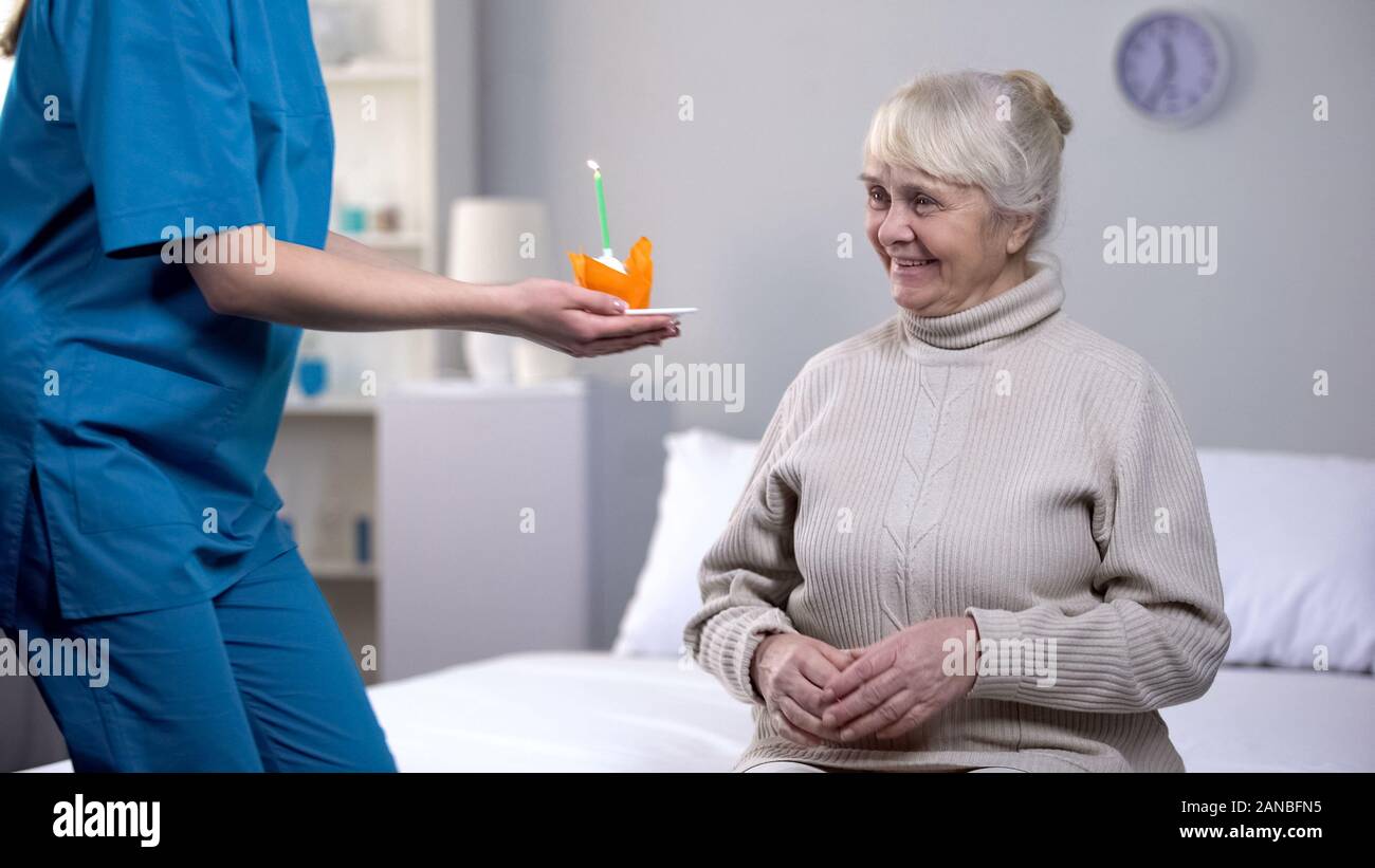 Tipo infermiere dando la torta di compleanno di età compresa tra lonely donna, avendo cura in età avanzata Foto Stock
