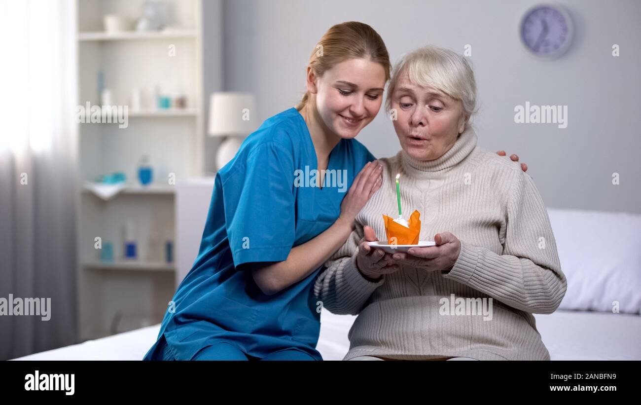 Volunteer abbracciando anziana signora soffiando candela sulla torta di compleanno e servizio ospedaliero Foto Stock