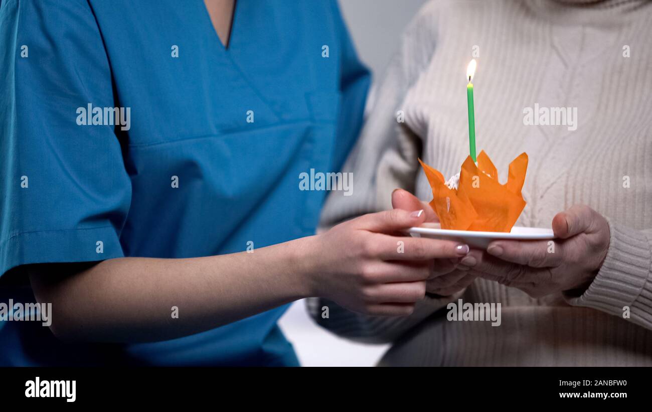 Volontari e donna anziana holding torta di compleanno, celebrazione in casa di cura Foto Stock