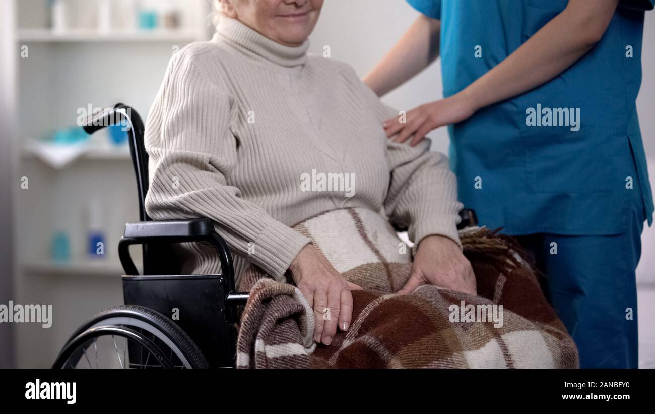 L'infermiera avendo cura circa donna anziana in carrozzina coperto da una coperta, ospedale Foto Stock