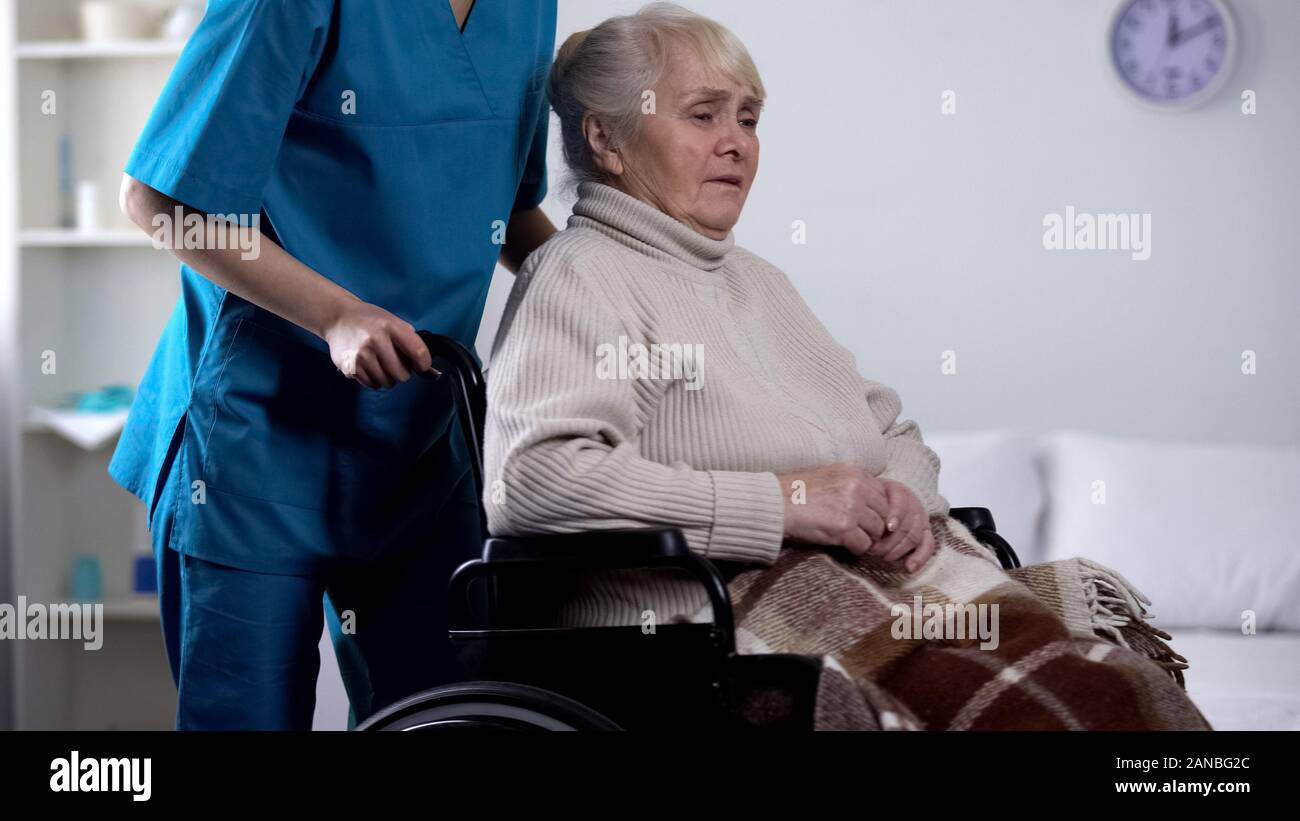 Lavoratore medico cura circa sconvolto senior lady in carrozzella, riabilitazione Foto Stock