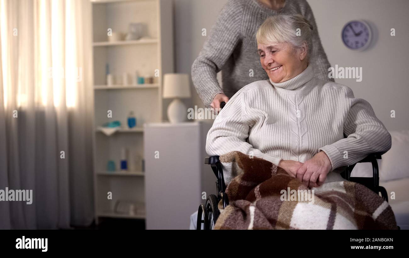 Figlia di prendersi cura di anziani madre in carrozzella, il caregiver ad aiutare il paziente Foto Stock