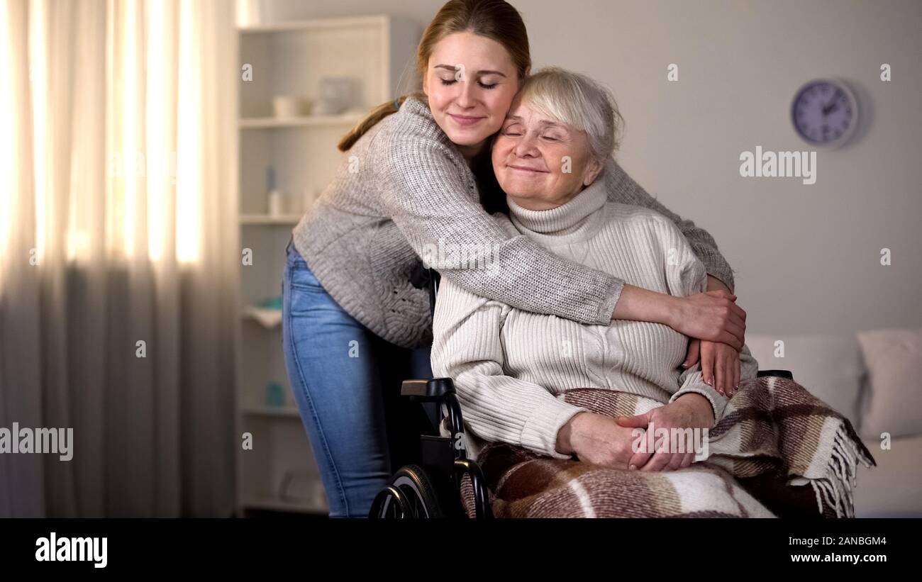 La nipote abbracciando sorridente vecchia donna in carrozzella, famiglia amore e cura Foto Stock