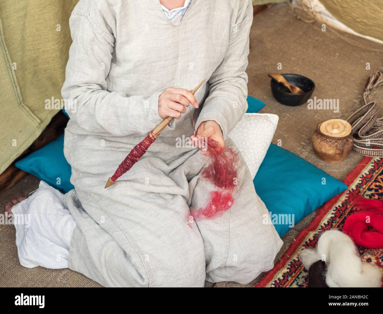La donna nel medioevo in abito di cotone la filatura con una ruota. Signora fa da filati di lana di pecora. Mandrini a mano. Ruota di filatura. La filatura. Procedimento Foto Stock