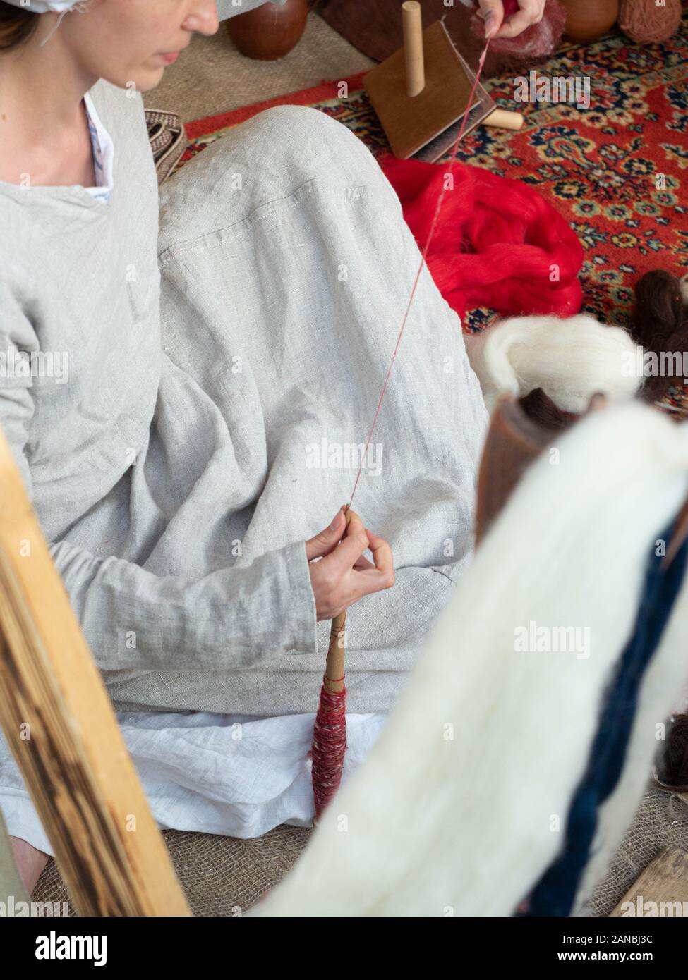 La donna nel medioevo in abito di cotone la filatura con una ruota. Signora fa da filati di lana di pecora. Mandrini a mano. Ruota di filatura. La filatura. Procedimento Foto Stock