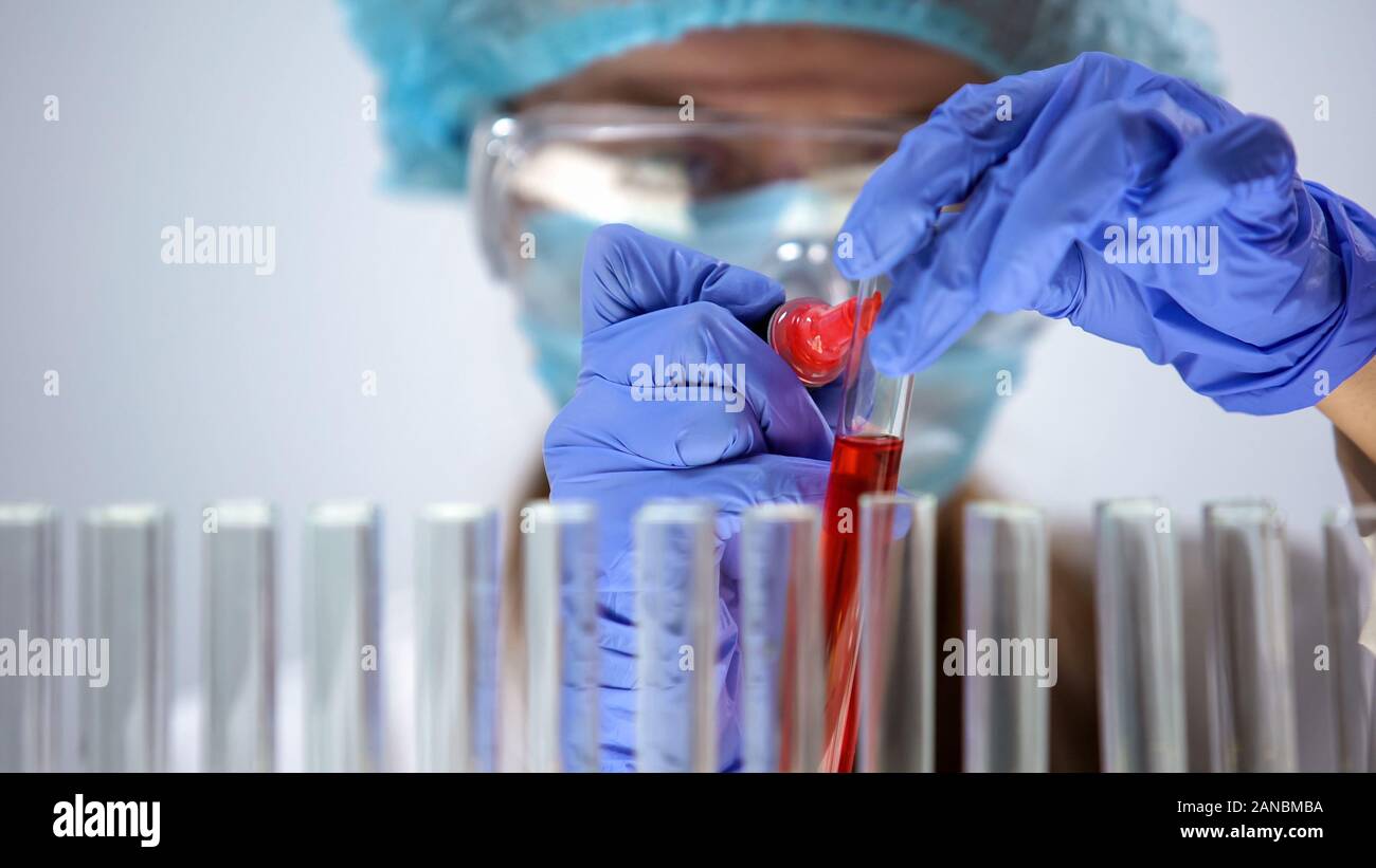 Scienziato tubo di marcatura con liquido rosso, condurre analisi campione, cosmetologia Foto Stock