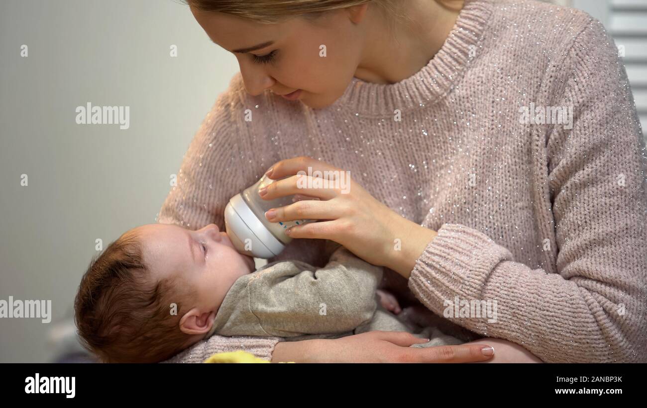 Giovane mamma alimentazione bambino più piccolo figlio dalla bottiglia, infant formula alimentazione artificiale Foto Stock