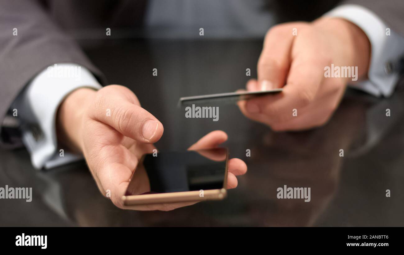 Società maschio manager digitando il numero della carta di credito smartphone, applicazione bancaria Foto Stock