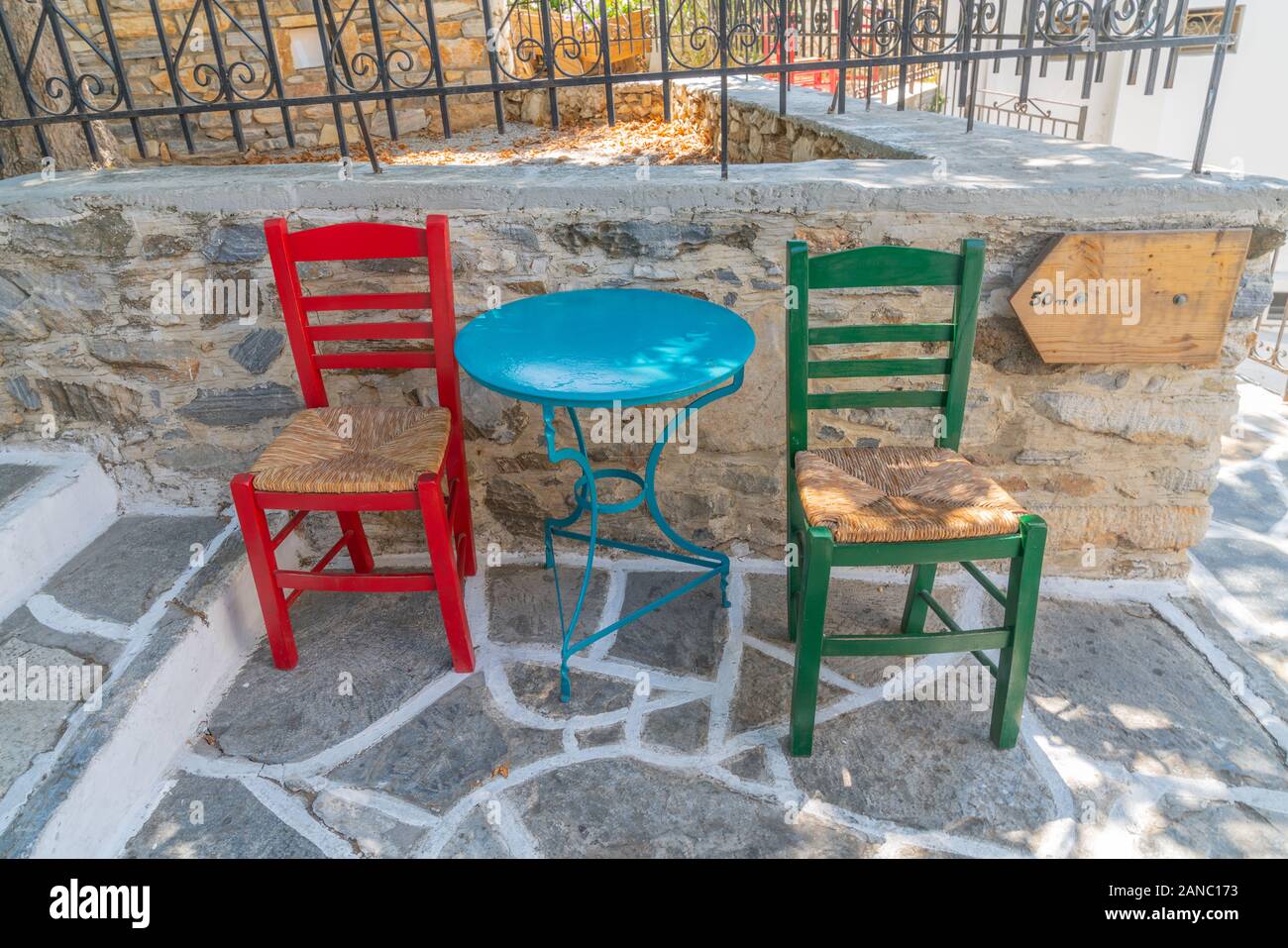 Due sedie vuote sul percorso del villaggio con tavolo blu e bianco cartello in legno nell'isola greca di villaggio in scena Filoti. Foto Stock