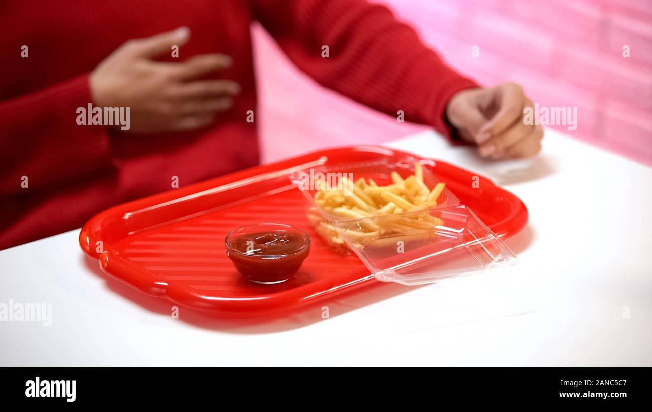 Sentimento donna mal di stomaco, patate fritte con ketchup sul tavolo, indigestione acida Foto Stock