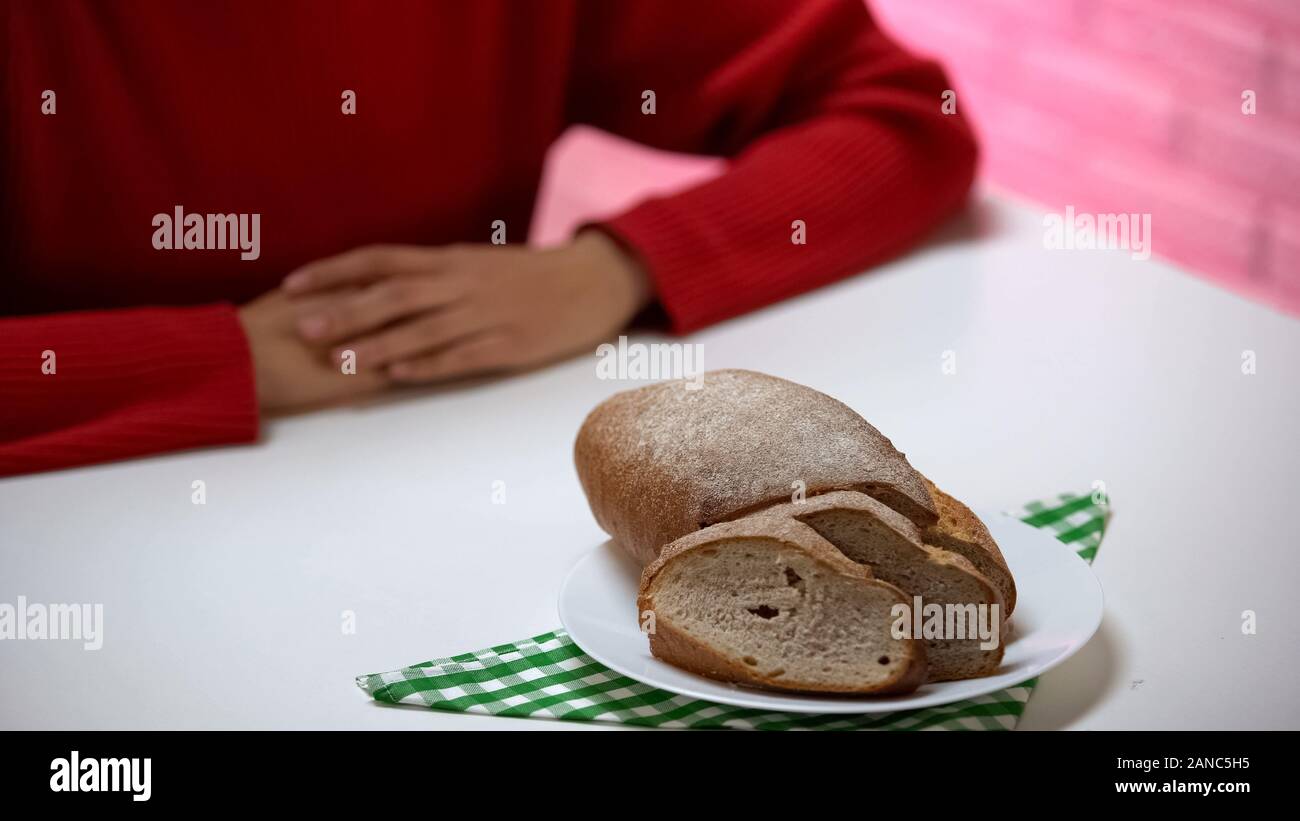 Pane giacente sulla piastra, donna seduta a tavola, rifiuta di mangiare ad alto contenuto calorico cibo Foto Stock