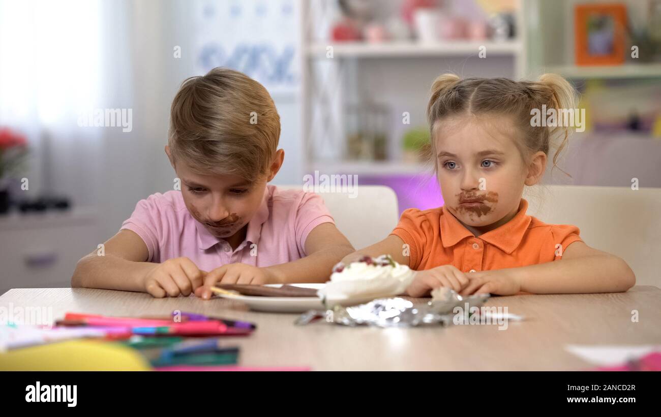 Maschio e femmina kids cosparse con cioccolato seduta a tavola, alimenti nocivi Foto Stock