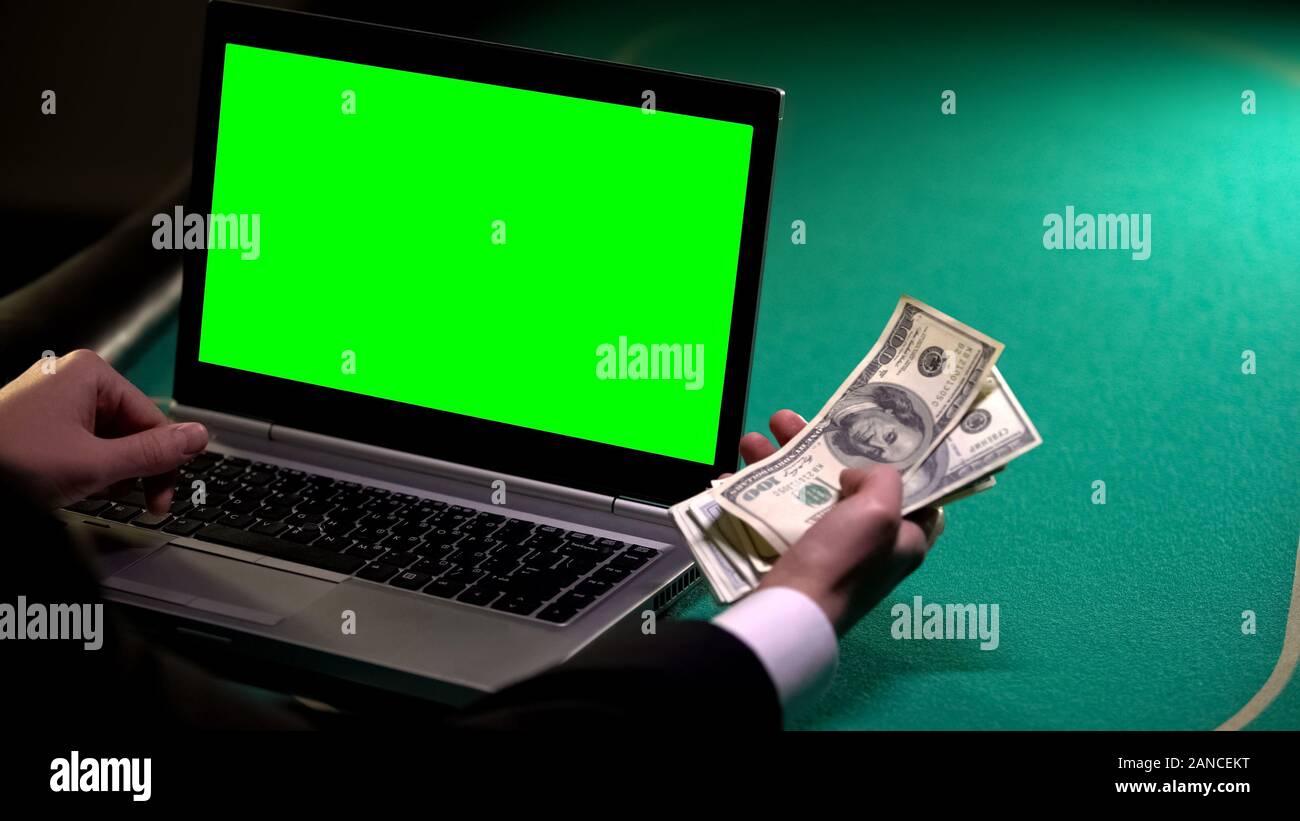 Maschio di giocare a poker online utilizzando laptop, tenendo le banconote di dollari, gioco d'azzardo Foto Stock