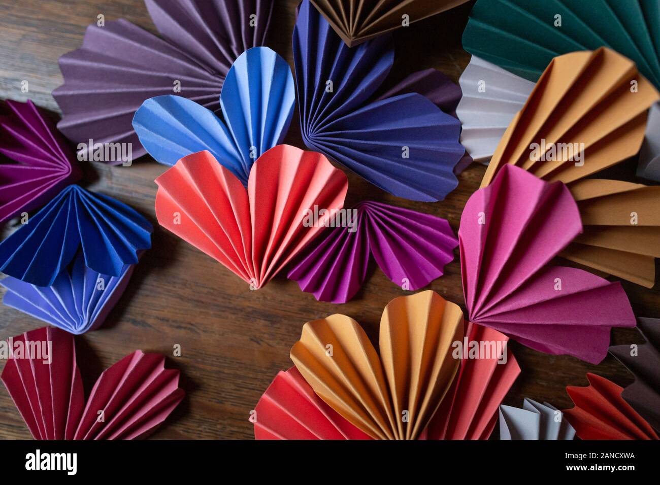 Cuori di origami di carta multicolore disposti su sfondo di legno Foto Stock