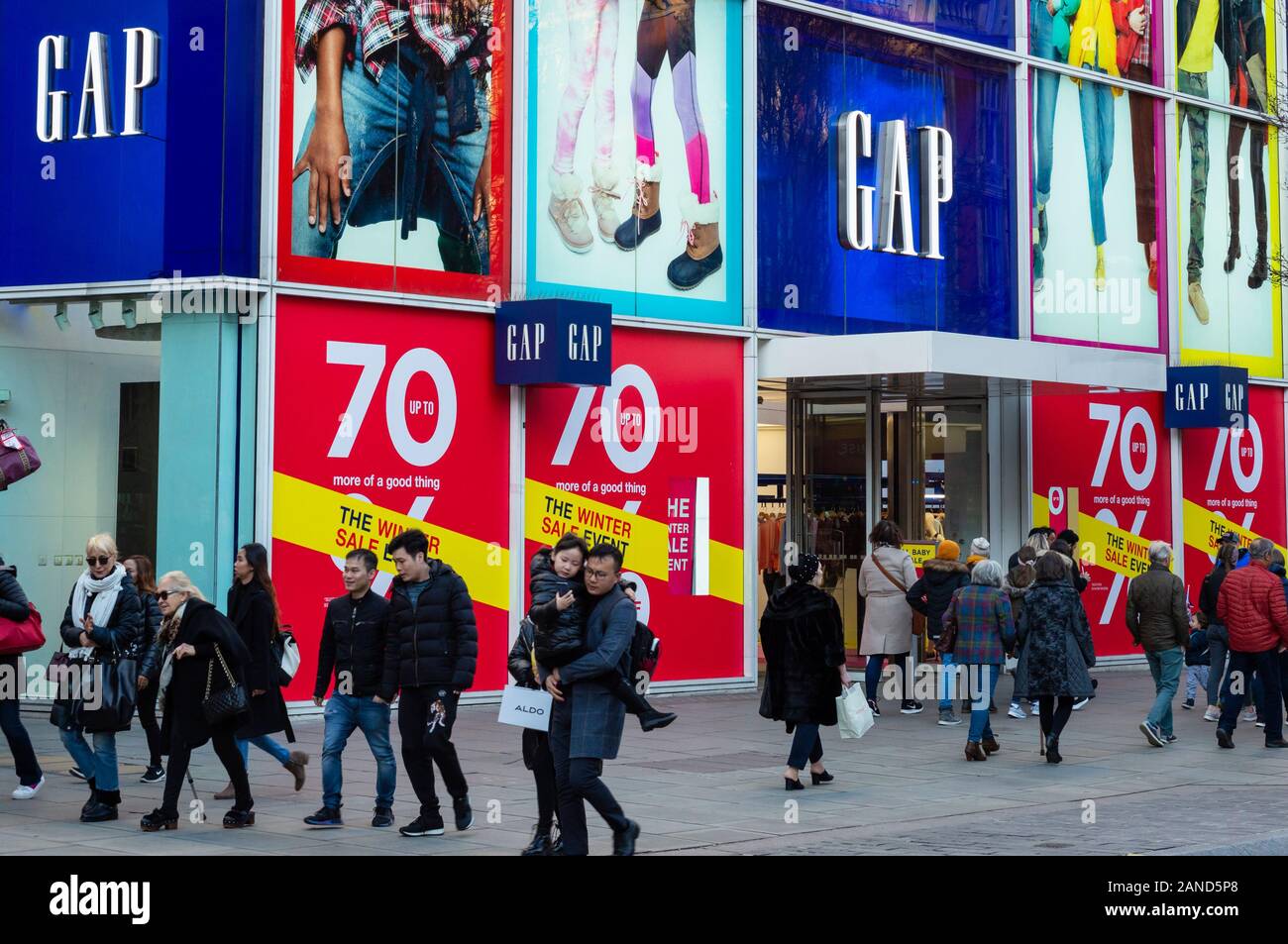 Acquirenti di Londra Oxford Street acquirenti di Londra persone che passano accanto ai grandi magazzini GAP colorato shopping front che offre il 70% di sconto di vendita, come visto nel gennaio 2020 a Oxford Street, Londra, Regno Unito Foto Stock