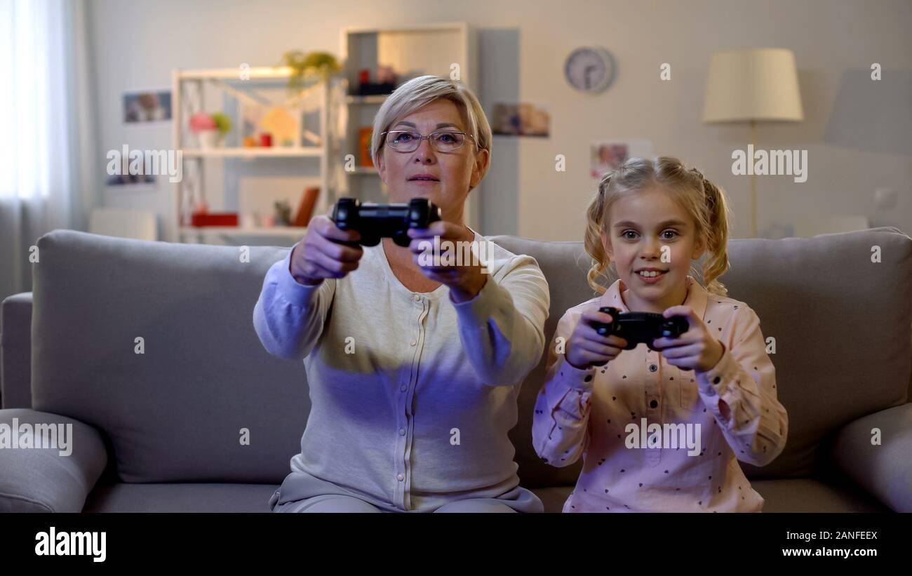 Ragazza carina e moderna granny riproduzione di video gioco a casa con il joystick, tempo libero Foto Stock