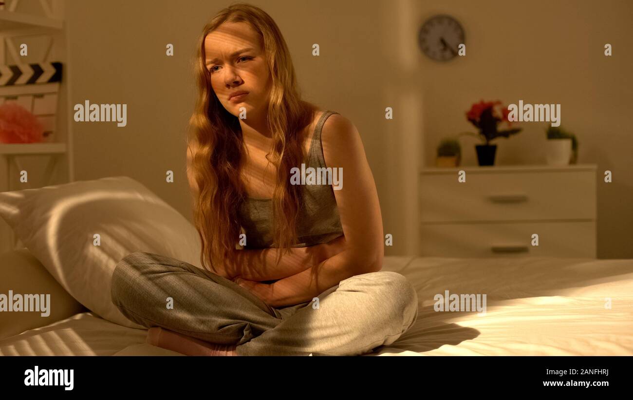 Giovane donna sensazione forte dolore nel dolore di stomaco seduta sul letto, healthcare Foto Stock