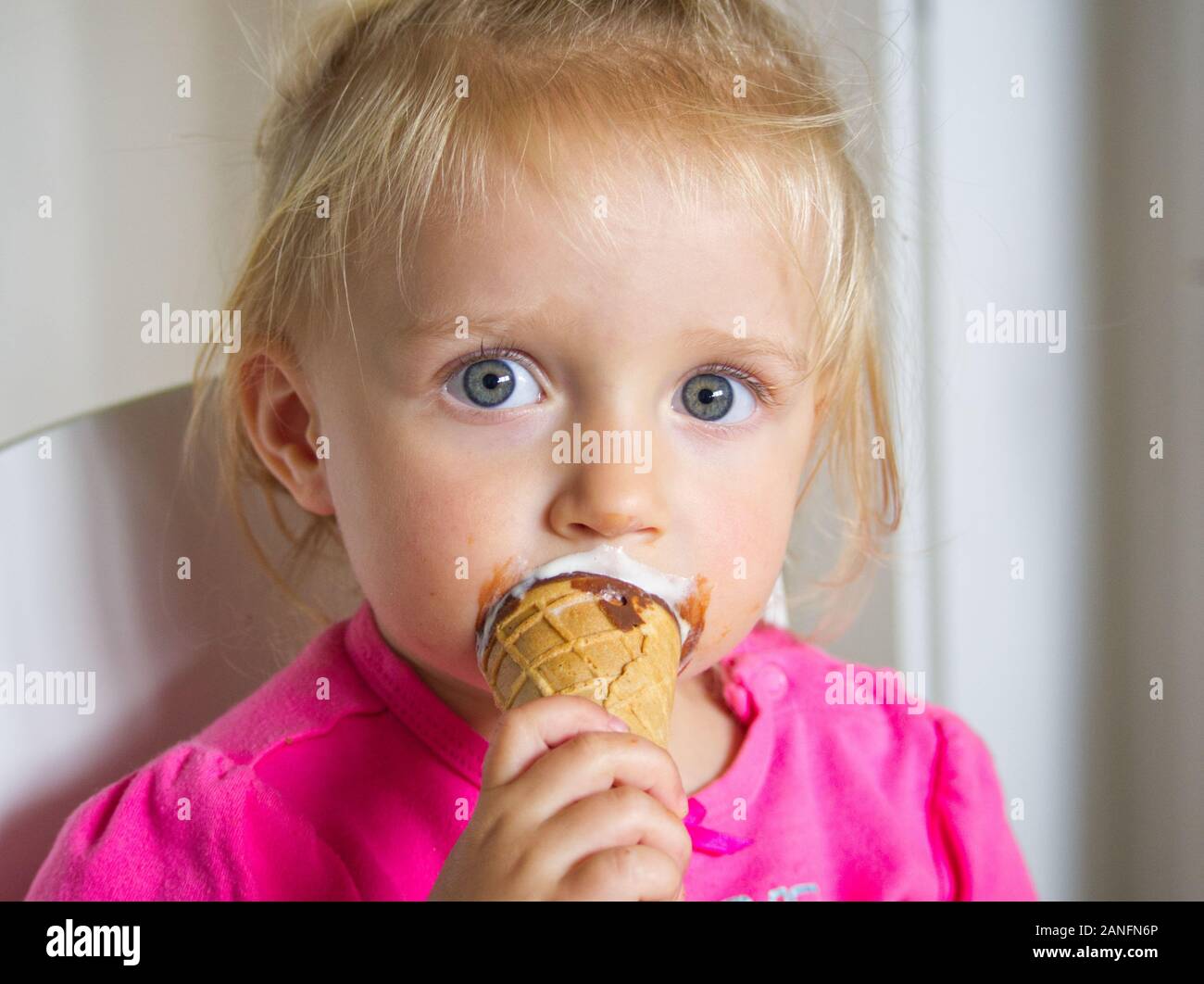 Giovane bambina con ampia aprire gli occhi blu e capelli biondi a mangiare il gelato Foto Stock