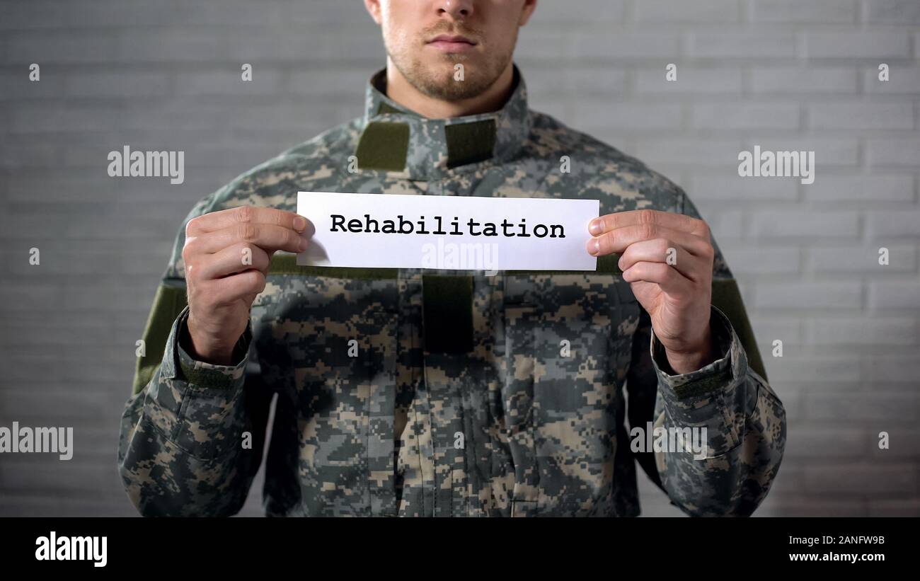 Parola di riabilitazione scritto il segno nelle mani del soldato maschio, assistenza sanitaria Foto Stock