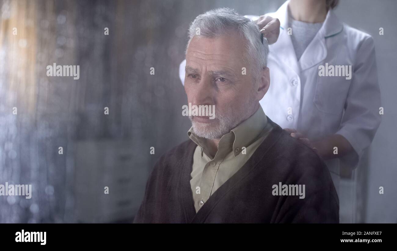 Il caregiver pettinatura di vecchio uomo capelli, infermiere avendo cura di lonely pensionato in ospizio Foto Stock