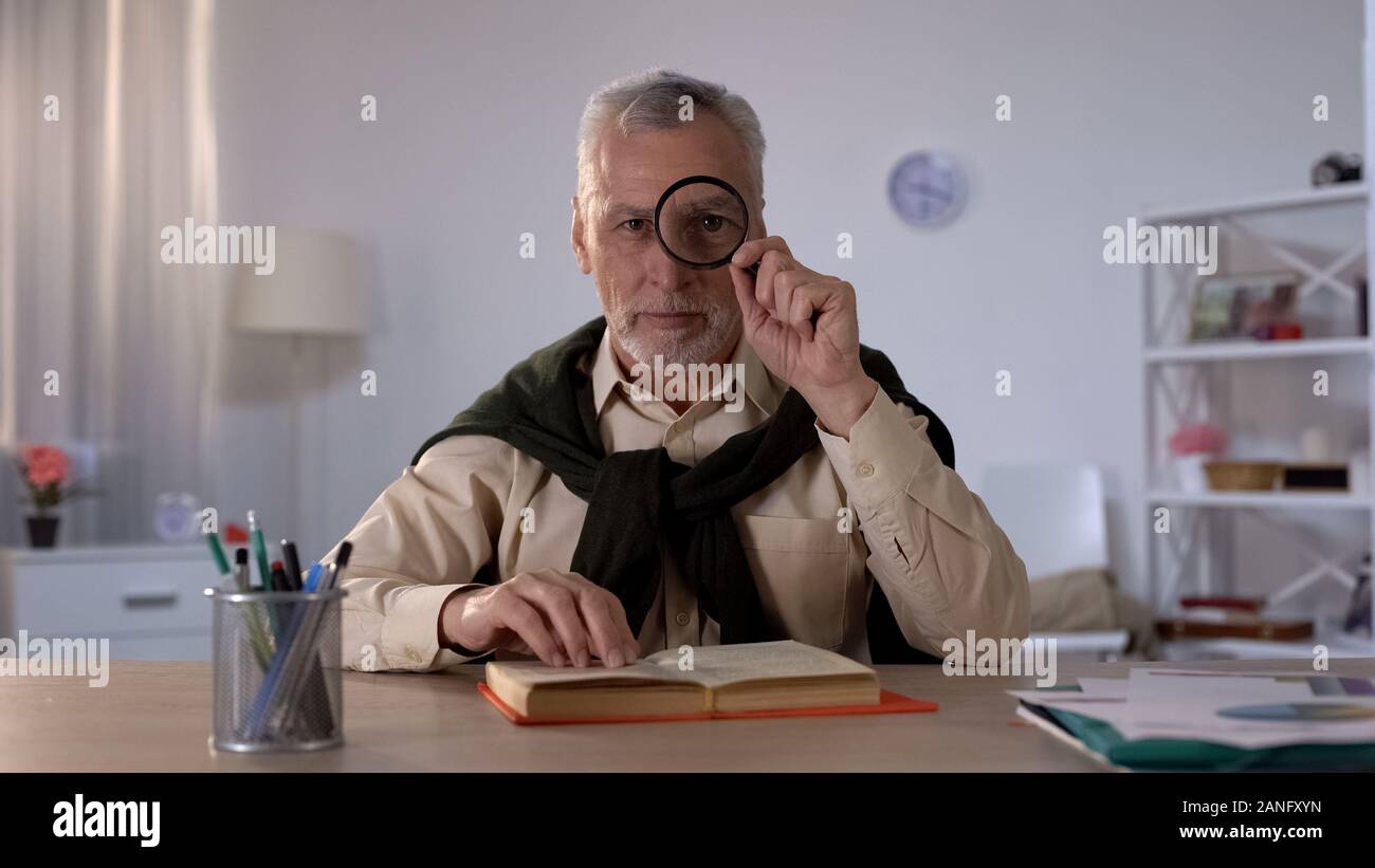 Il vecchio uomo cerca attraverso la lente di ingrandimento, tempo libero con piacere, occhio ingrandita Foto Stock