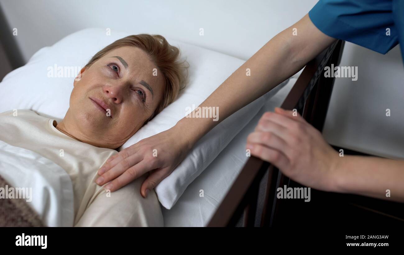 Tipo medic holding vecchia spalla femminile, senior paziente sdraiato in sickbed, rehab Foto Stock