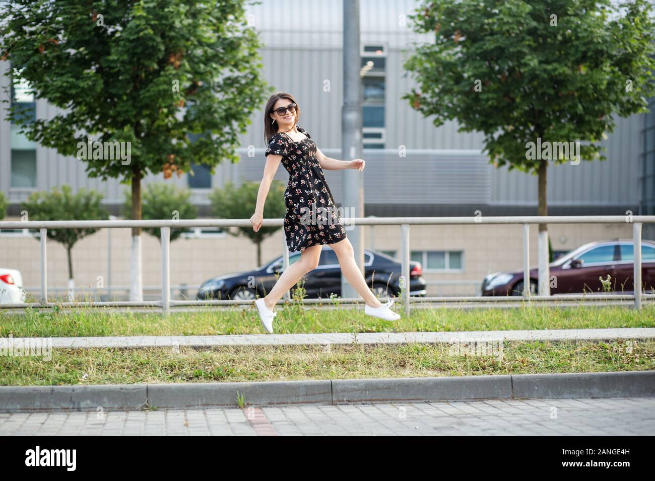 Adulto brunette donna correndo giù per la strada in un elegante abito. Il concetto di uno stile di vita urbano, la felicità e la vita attiva. Foto Stock