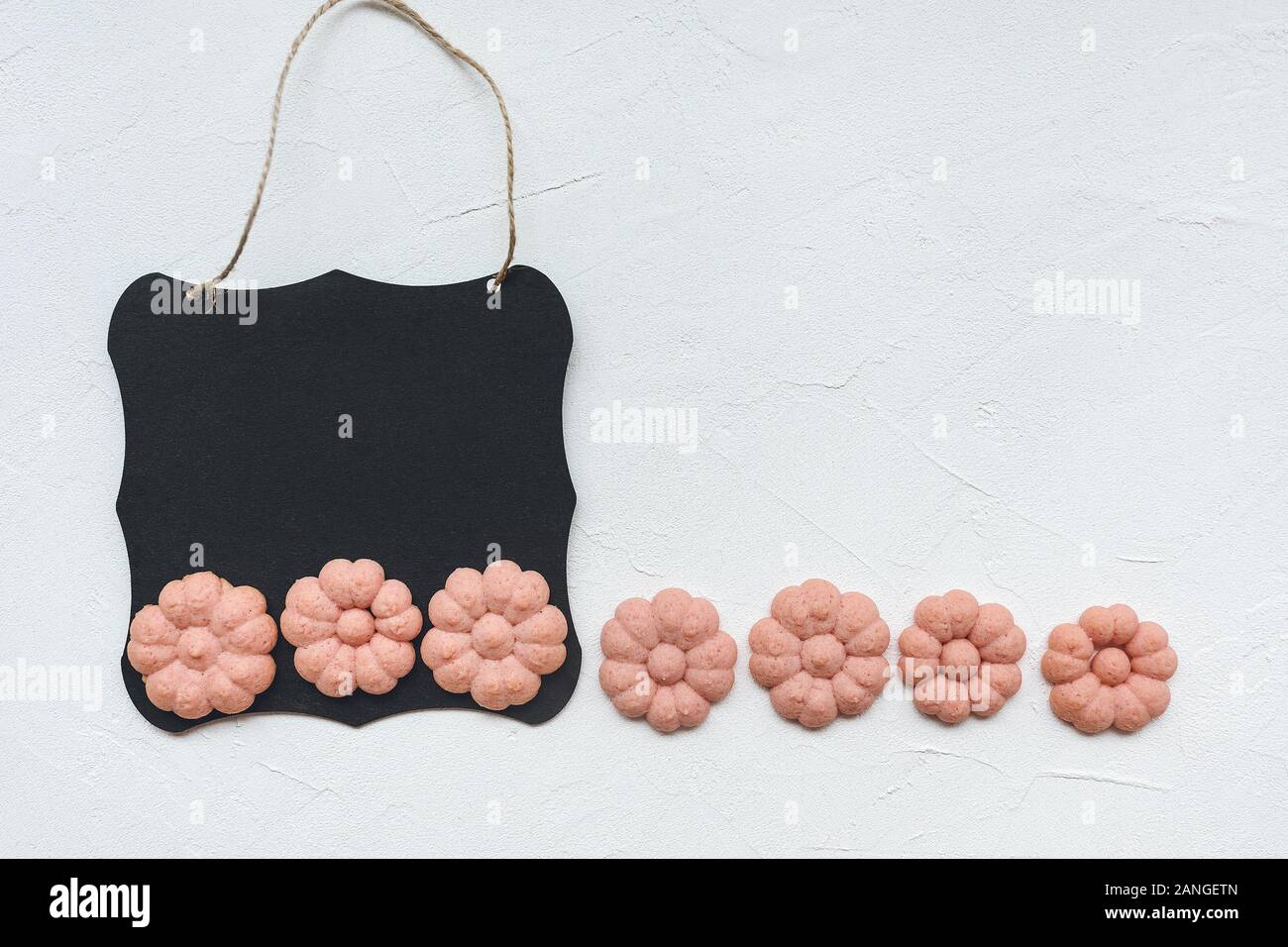 Lavagna nera e a forma di fiore i cookie su uno sfondo bianco, copyspace. Vista superiore, piana, laici mockup. La primavera e a Pasqua shopping, la cottura e la lista Da fare Foto Stock