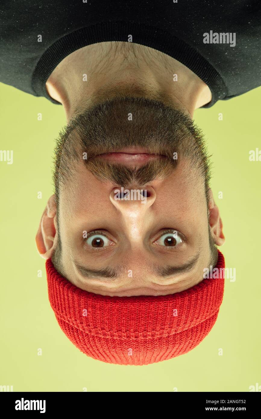 Carino sorridente. Verticale invertito di soggetti di razza caucasica giovane uomo su giallo di sfondo per studio. Le emozioni umane non sono quello che sembrano quando stai guardando. L'espressione del viso, funny view, pubblicità. Foto Stock