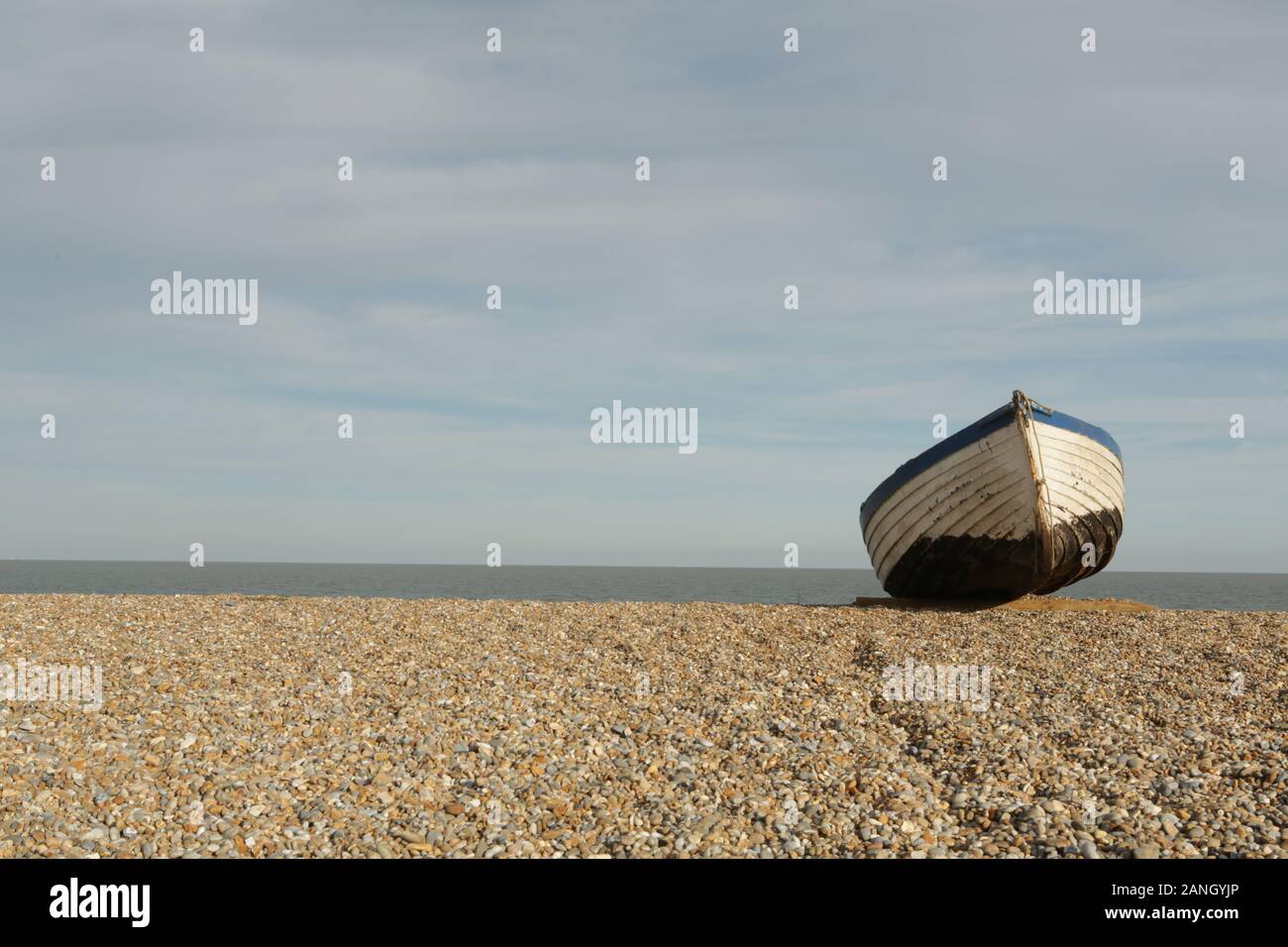 Una barca a sinistra sulla spiaggia di ghiaia a Suffolk, East Anglia, Inghilterra Foto Stock
