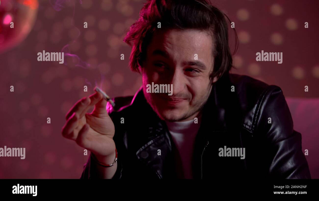 Maschio intossicato guardando la cannabis sigaretta, della dipendenza da droghe e alcool Foto Stock