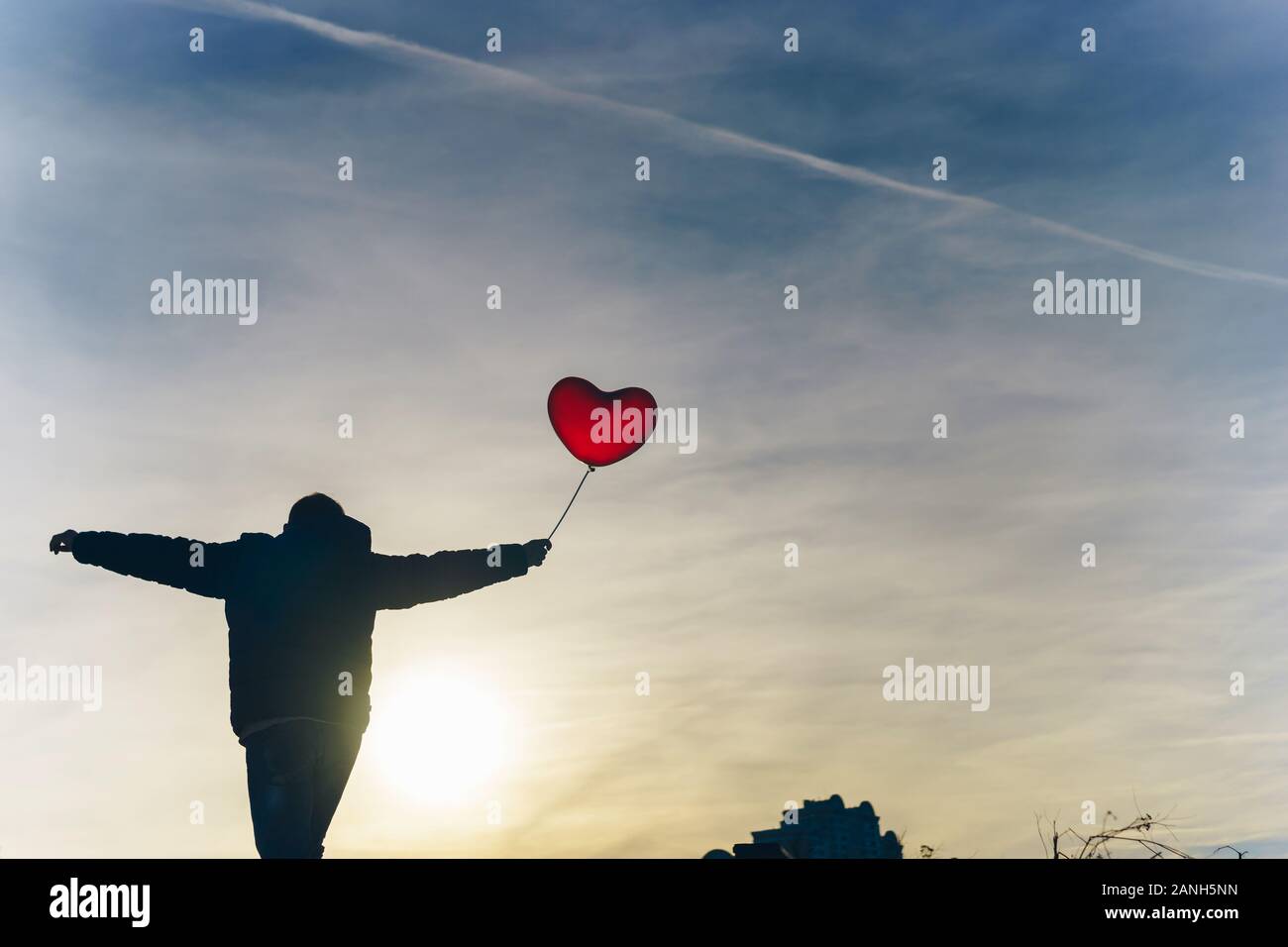 L uomo dal retro con un palloncino rosso in mano contro il cielo blu su frosty giorno Foto Stock