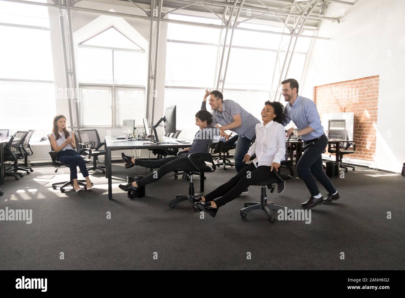 Emozionato millenario lavoratori diversi divertirsi in office racing su sedie insieme, felice multirazziale dipendenti impegnati in attività di team building, laughin Foto Stock
