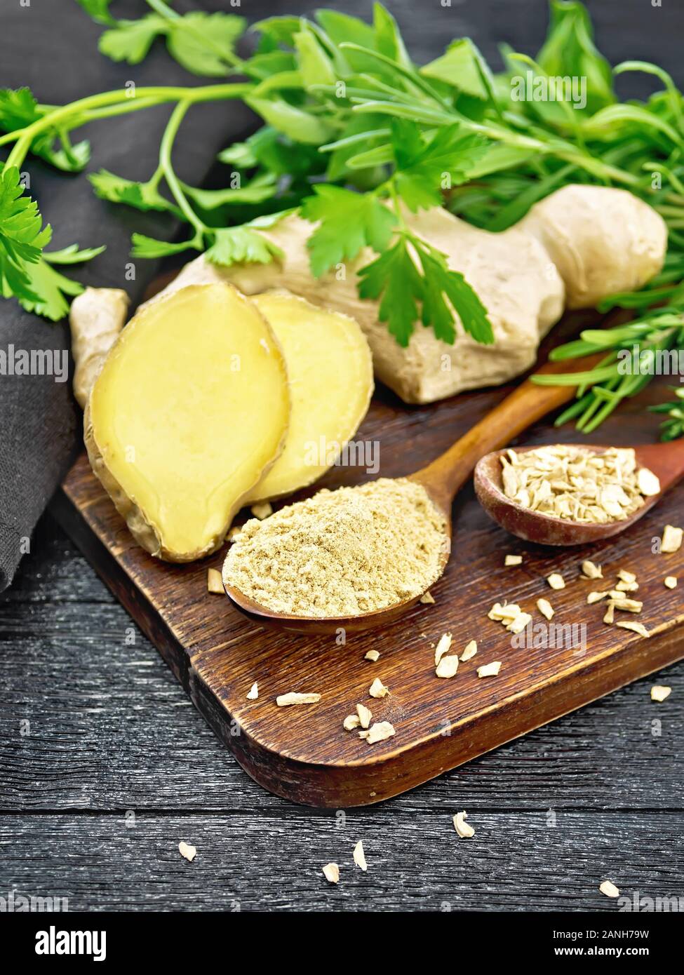 Lo zenzero in polvere e scaglie in due cucchiai di legno, radice di zenzero, erbe aromatiche su un di legno nero lo sfondo della scheda Foto Stock