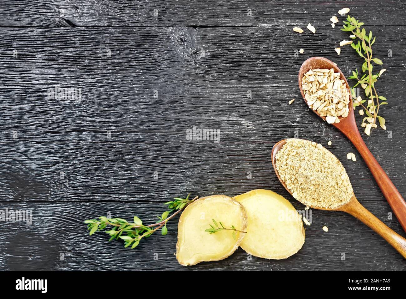 Telaio di zenzero in polvere e cereali secchi in cucchiai, due fette di radice di zenzero, rametti di timo in un legno nero superiore della scheda Foto Stock
