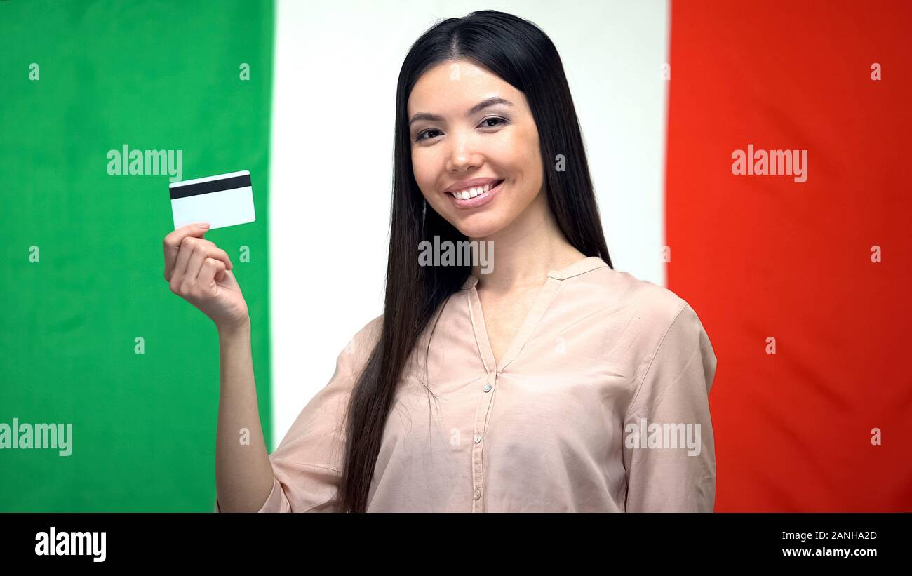 Donna positiva tenendo carta di credito contro la bandiera italiana, il servizio Trasferimento di denaro Foto Stock