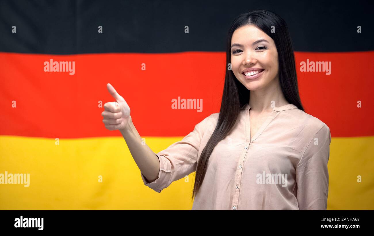 Bella femmina Asiatica che mostra pollice in alto segno contro la bandiera tedesca sullo sfondo Foto Stock
