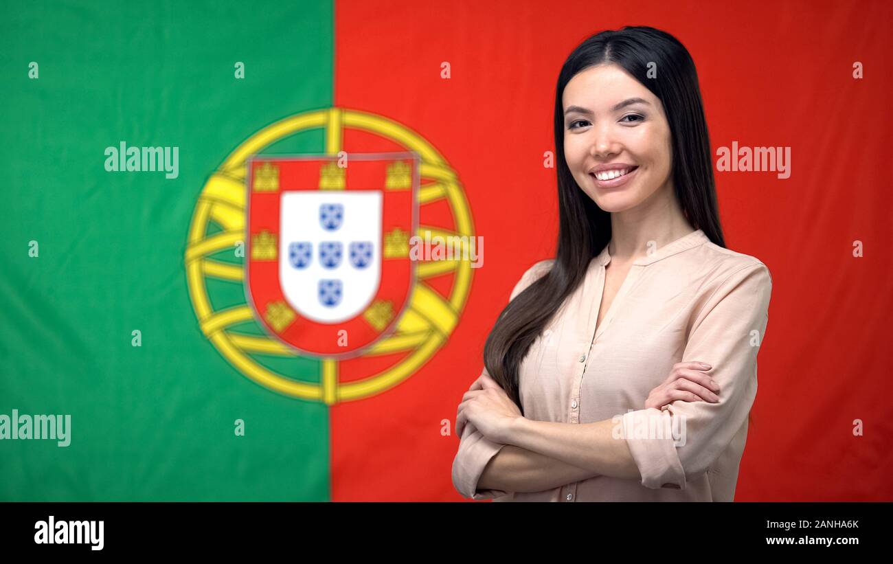 Donna sorridente in piedi con le mani incrociate contro la bandiera portoghese sfondo Foto Stock
