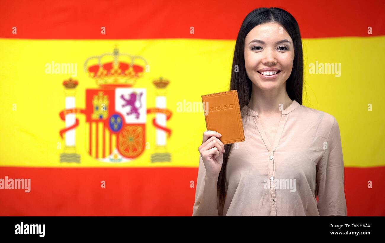 Sorridente ragazza asiatica holding passaporto contro Spanish flag di sfondo, cittadinanza Foto Stock