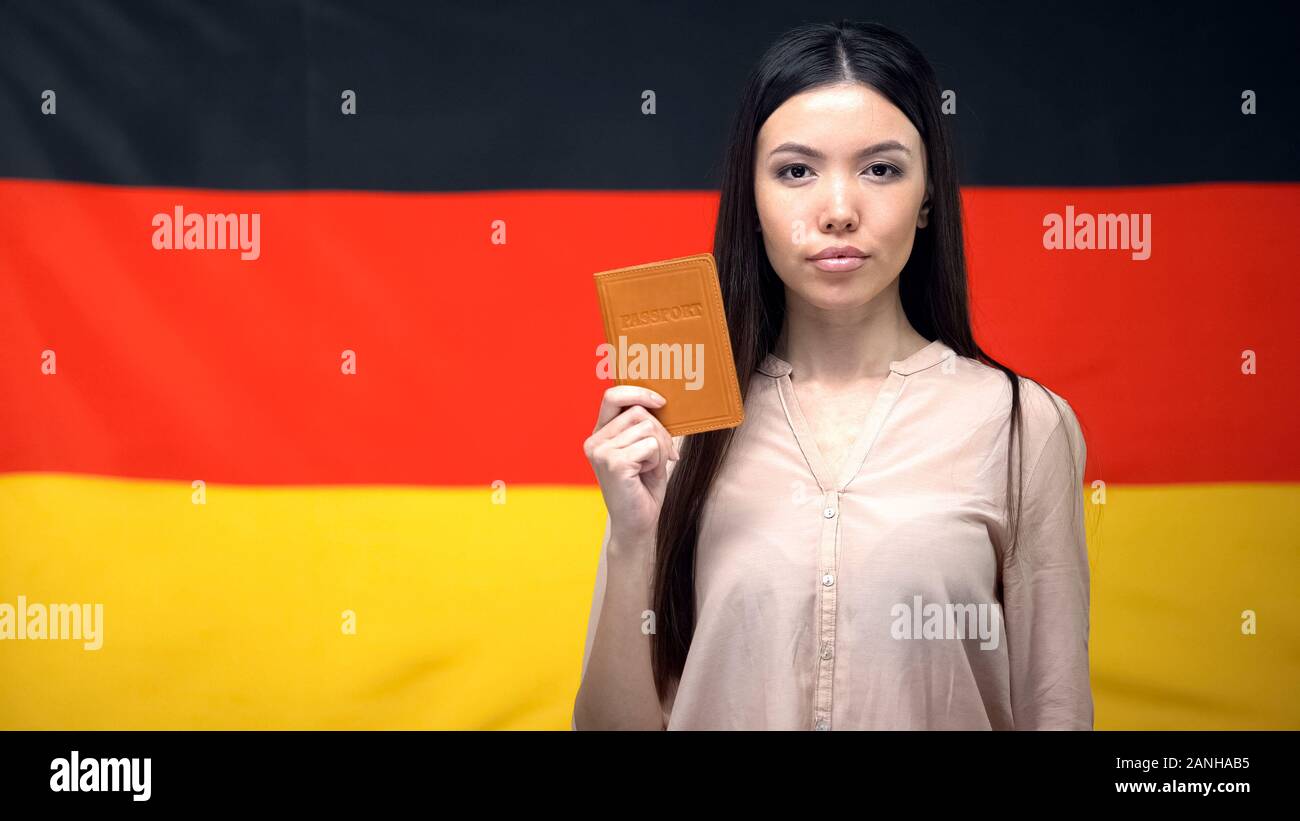 Grave femmina asiatica mostrando passaporto contro bandiera tedesca sfondo, close-up Foto Stock