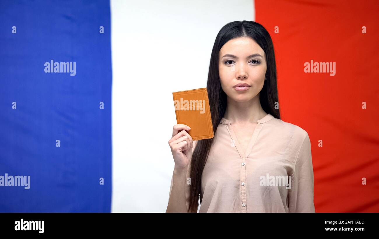 Grave femmina asiatica mostrando passaporto contro bandiera francese sfondo, Embassy Foto Stock