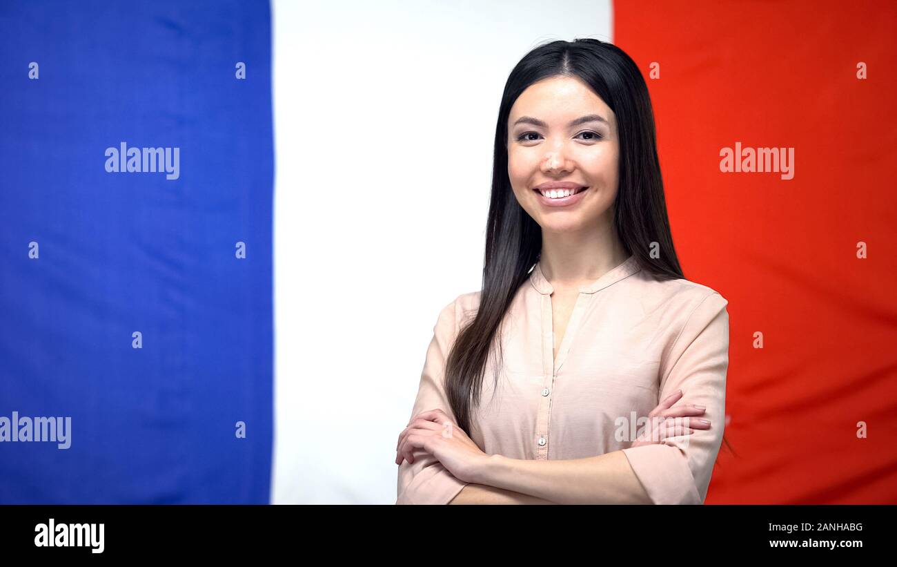 Allegro ragazza asiatica in piedi con le mani incrociate contro la bandiera francese sullo sfondo Foto Stock
